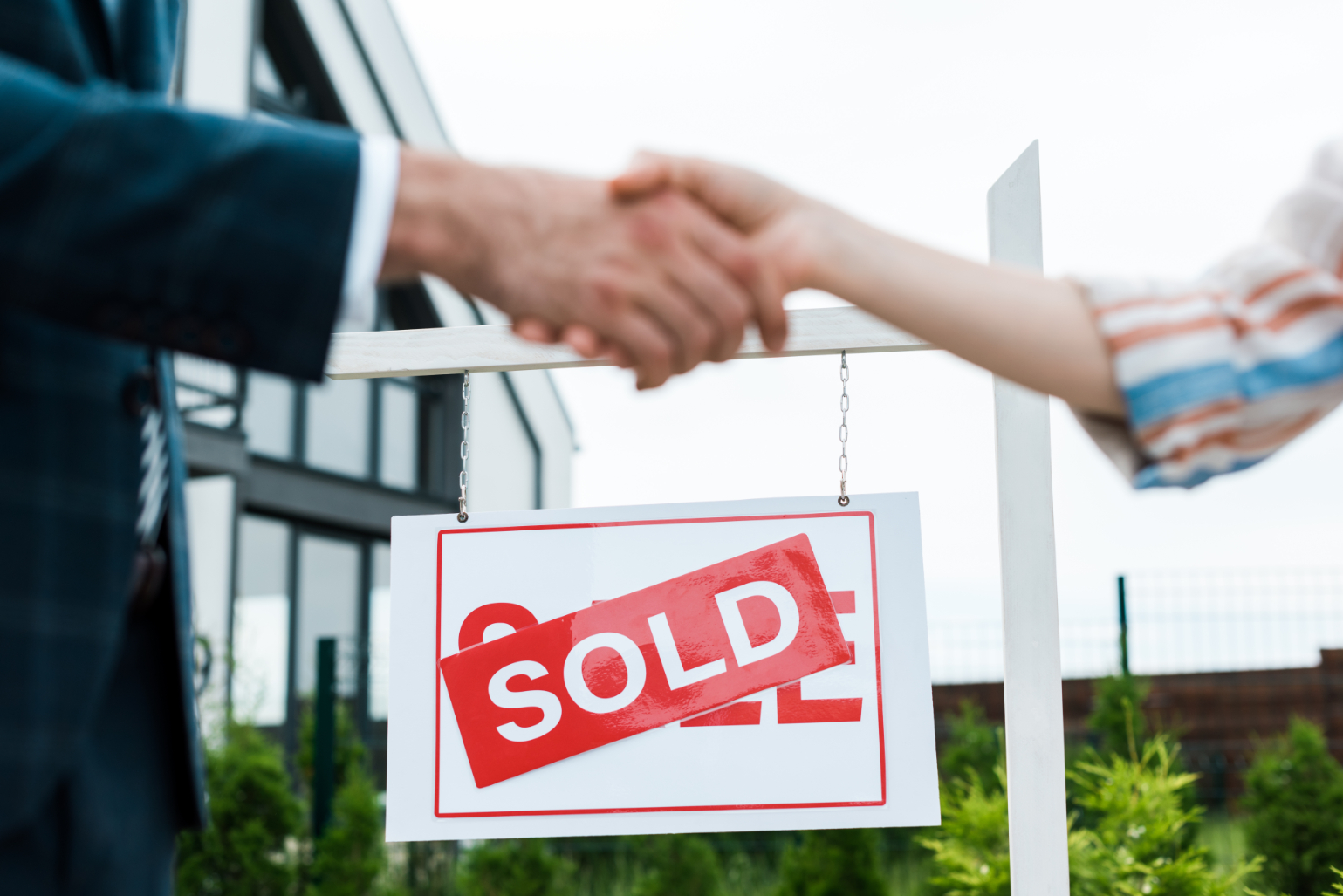 Realtor shaking hand of client in front of sold sign